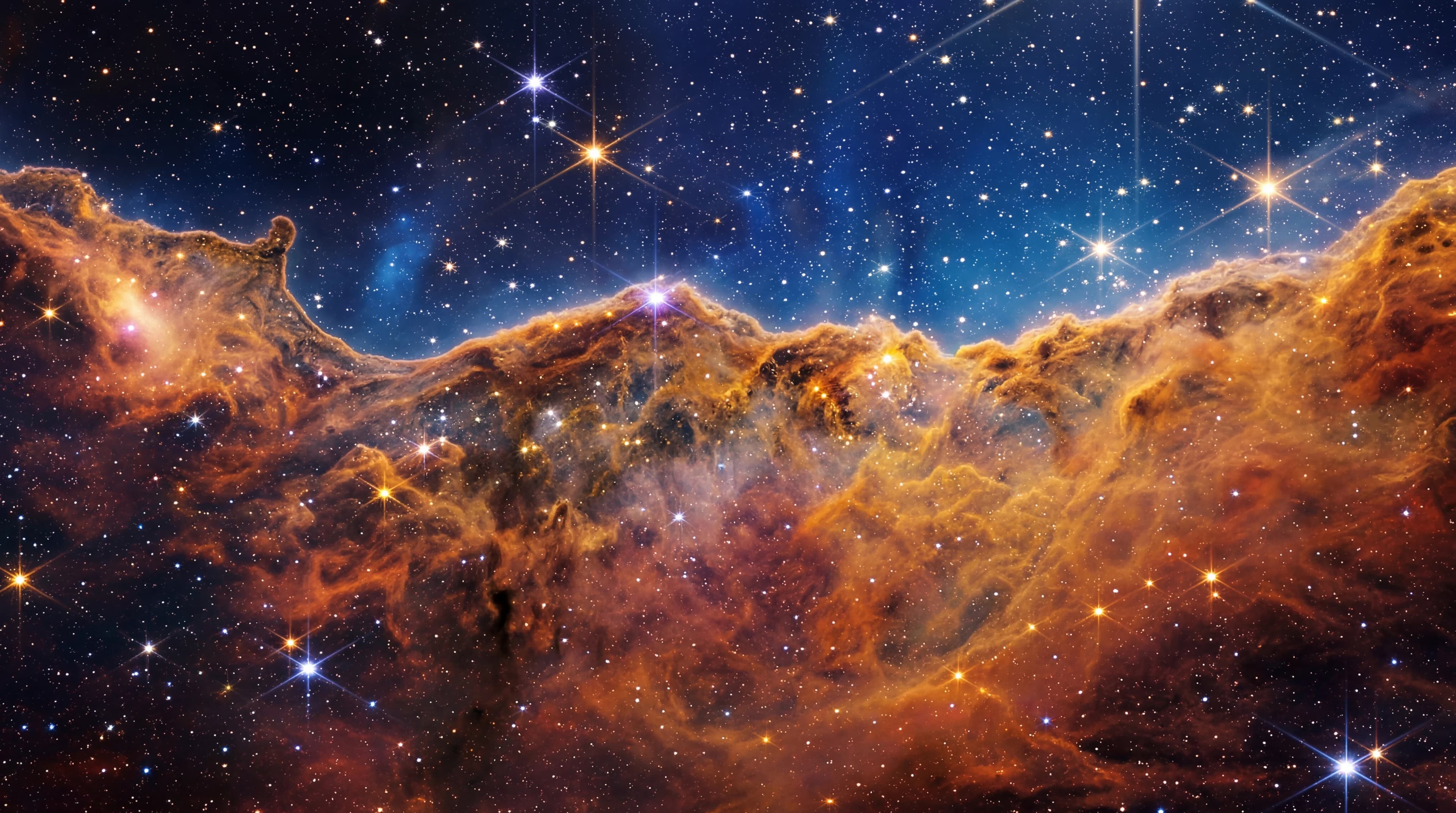 Deep space panorama with warm gold nebula clouds against dark indigo void, scattered stars